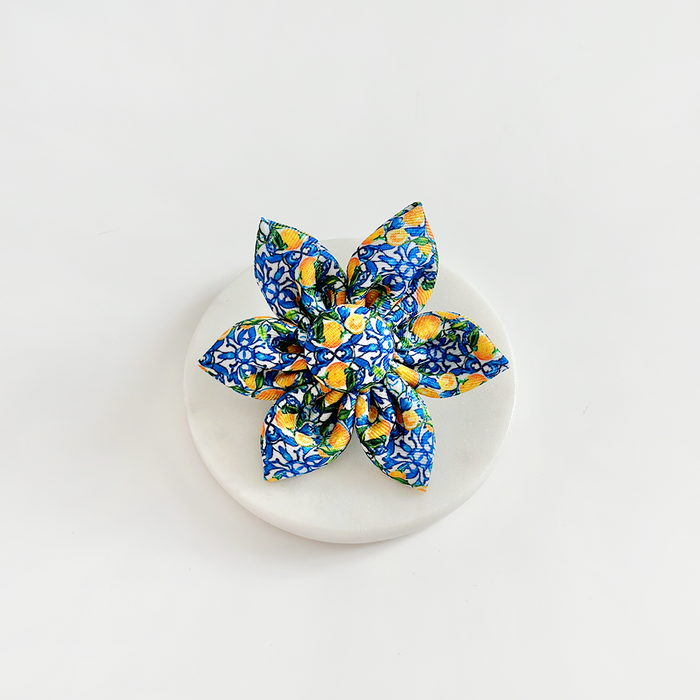 Yellow lemon-patterned fabric collar flower by Cocopup London on a round white surface with a plain white background.