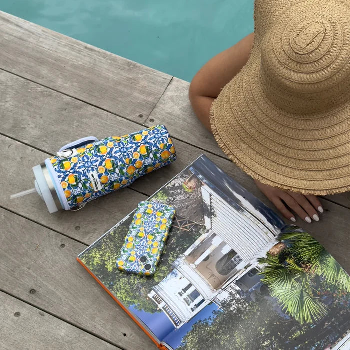 Person in a straw hat reads poolside next to a yellow lemon-patterned tumbler carry case.
