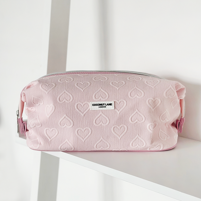 Light pink makeup bag with heart pattern by Cocopup London, shown on a white shelf.