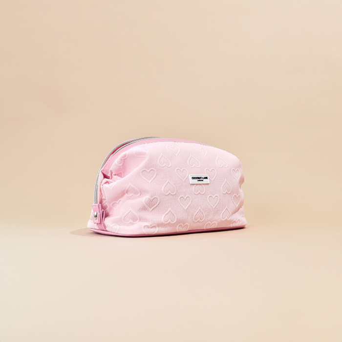 Baby pink expandable makeup bag with heart pattern and front label, shown on a beige background.