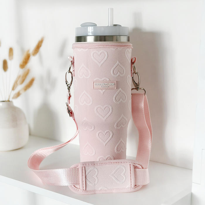 Baby pink tumbler carry case with heart pattern, holding a straw tumbler, displayed on a white shelf.