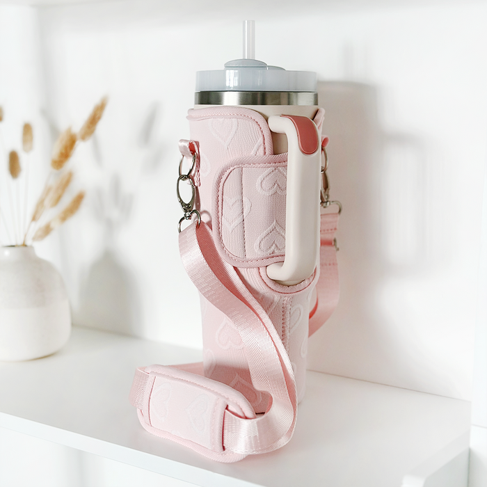 Baby pink tumbler carry case with heart pattern and straw, displayed on a white shelf.