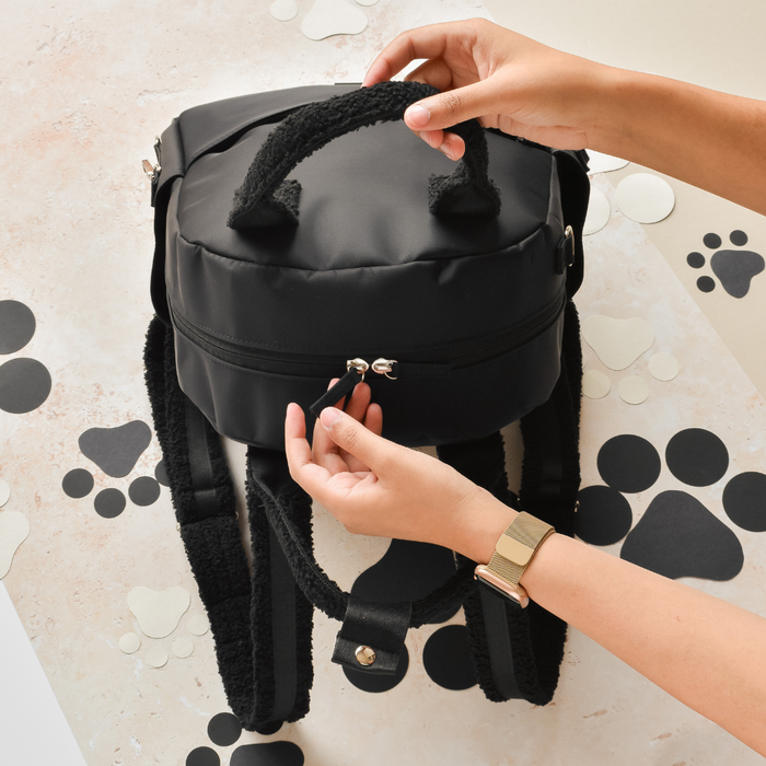 Black Cocopup London rucksack with furry handles, opened by hands, surrounded by black and beige paw print cutouts.