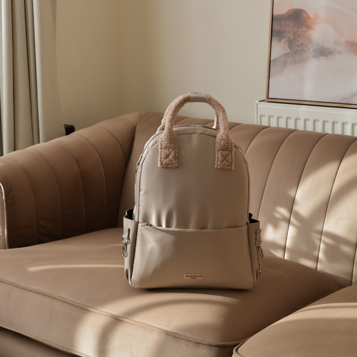 Caramel Latte Cocopup London rucksack with fuzzy handles on a tan sofa in soft indoor light.