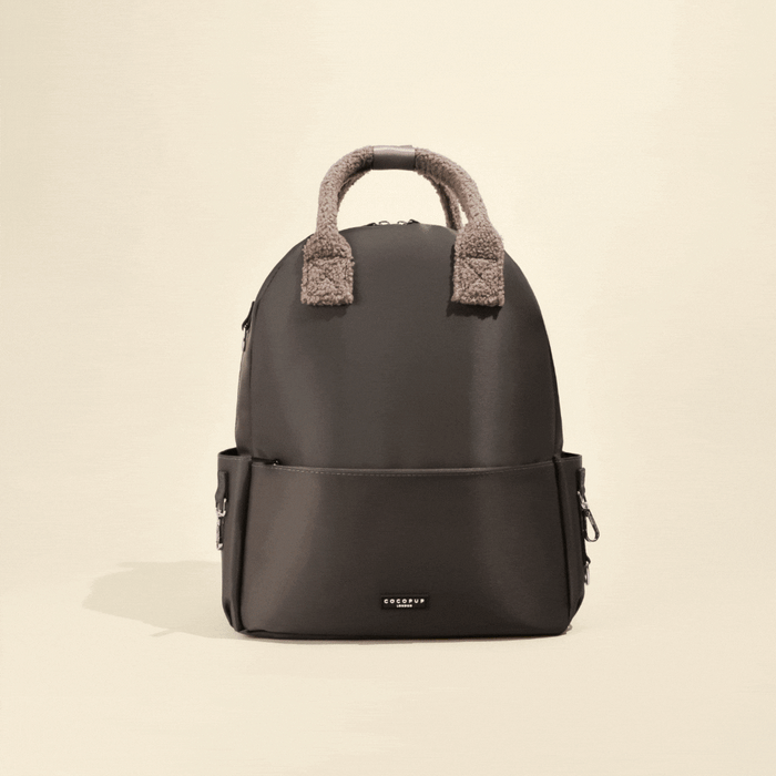 Mocha rucksack with shearling top handles, zip closure, and side pockets on a cream background.
