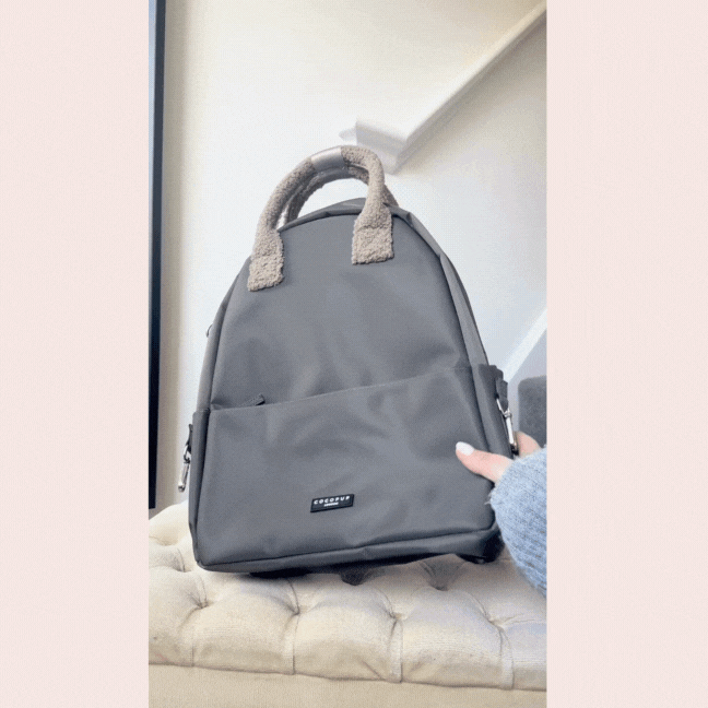 Mocha rucksack with fluffy teddy handles, front pocket, and silver zippers, displayed on a cushioned seat.