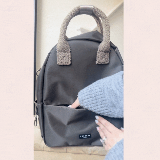 Hand reaching into front pocket of mocha Cocopup London rucksack with fluffy teddy fabric handles.