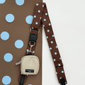 A brown bag strap with light blue polka dot design. Attached is a beige small pouch for dog treats.