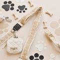 A beige dog leash with a faux fur lining is attached to the Bag Strap - Quilted, featuring the "Cocopup London" label. It is displayed on a light background decorated with paw print and bone shapes. Additional bones and a collar are scattered around, making it ideal for your Cocopup dog walking bag.