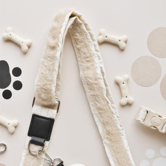 A fluffy beige dog leash from Cocopup is surrounded by bone-shaped dog treats, circular cutouts in shades of beige, and a paw print design. The white buckle and metal clasp add functionality. Perfectly paired with the Cocopup London Bag Strap - Quilted or Dog Walking Bag for stylish strolls, the items rest on a light surface.