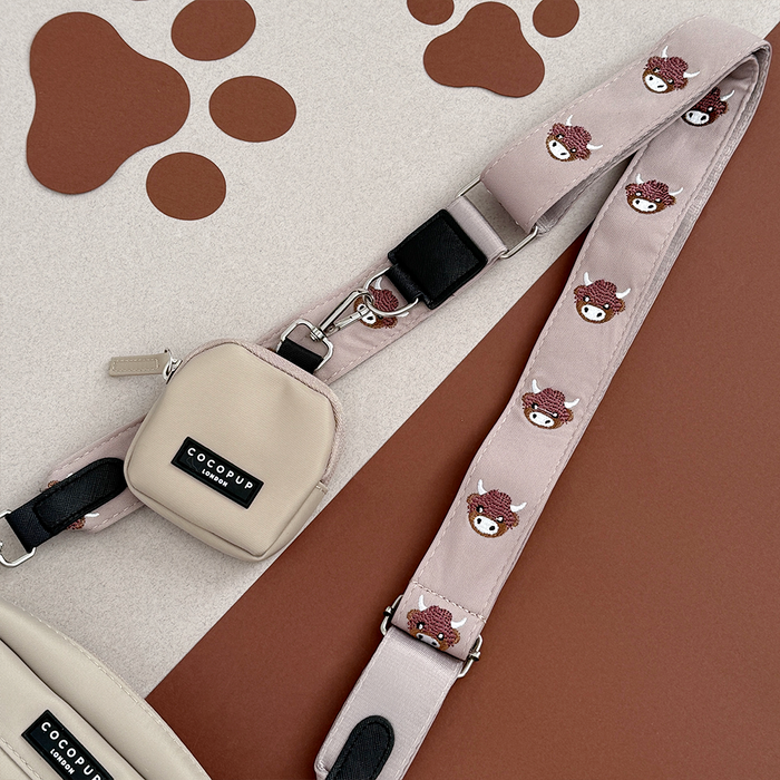 Beige and pink Cocopup London bag strap with paw prints, brown background, matching pouch attached.