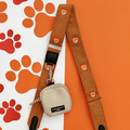 A brown / orange corduroy bag strap, with embroidered lion faces. Attached is a small beige pouch for dog treats.