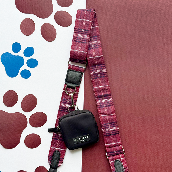 Maroon plaid dog leash with black pouch beside matching Mulberry Plaid bag strap on paw print fabric.
