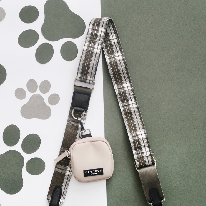Olive check bag strap with small beige pouch and black clasp, displayed on green paper with paw print pattern.