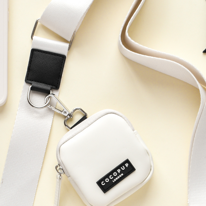 A small, polyester, square-shaped dog walking bag from Cocopup London features a label that says "COCOPUP LONDON" and is attached to an oyster white Bag Strap with a black patch and silver-tone hardware. The bag is laid flat against a light-colored background.
