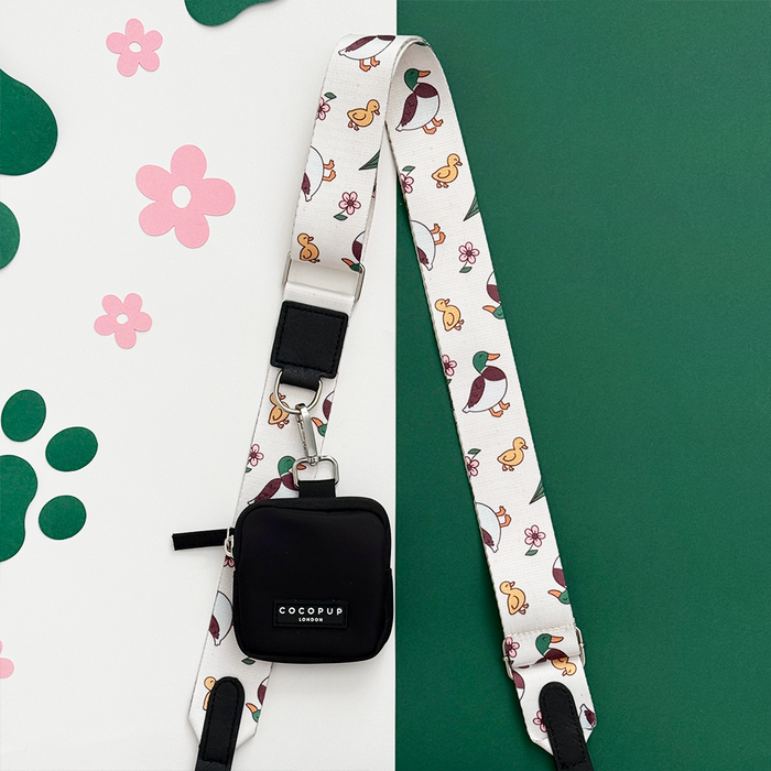 White Cocopup London bag strap with duck and flower pattern, paired with black pouch on paw print background.