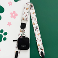 White Cocopup London bag strap with duck and flower pattern, paired with black pouch on paw print background.