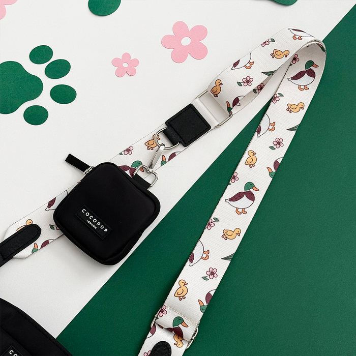 Cocopup London bag strap in Puddle Pup pattern with cartoon duck leash, black pouch, and paw print backdrop.