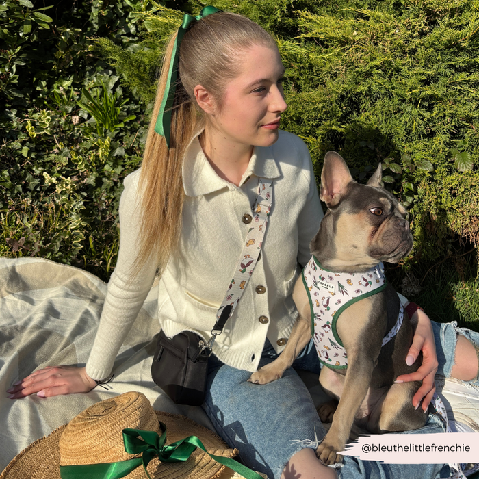 Blonde woman on a picnic blanket with her French Bulldog wearing a beige Cocopup London bag strap with brown spots.