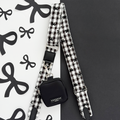 Cocopup London bag strap with black and white plaid pattern and attached black pouch, set on a bow-patterned background.