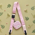 Pink quilted floral bag strap with a small matching pouch, displayed among green leaves and tiny white flowers.