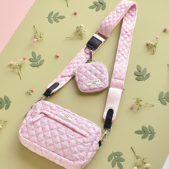 Quilted pink bag strap with a ditsy floral pattern, displayed on a green surface with small flowers.