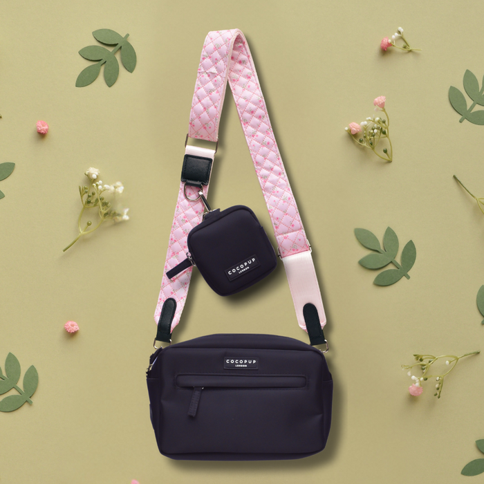Black crossbody Cocopup London dog walking bag with quilted ditsy floral pink strap, set among green leaves and small flowers.