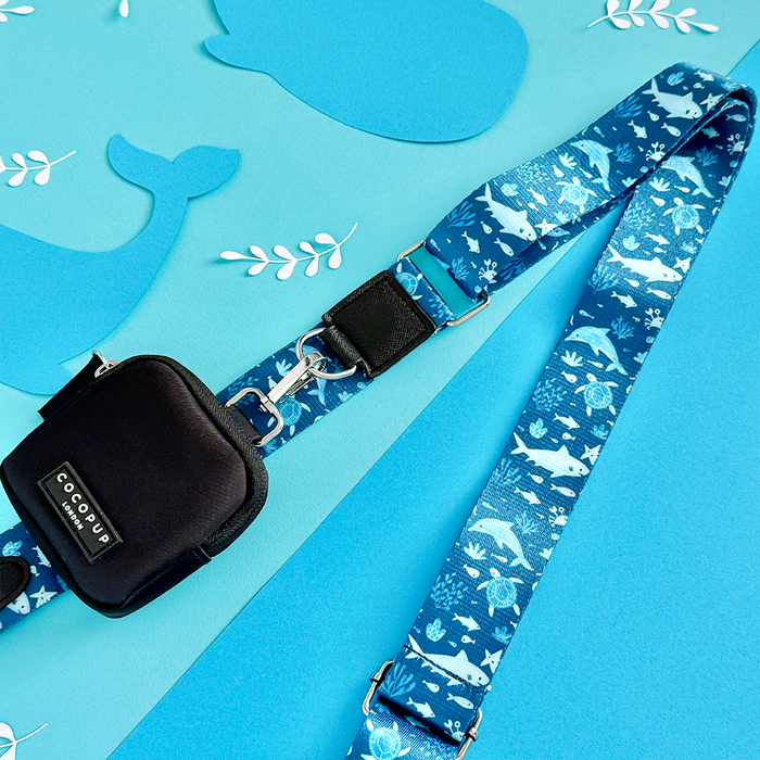 Blue Cocopup bag strap with white marine animal pattern, paired with a black pouch featuring whale cutouts.