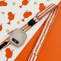 A orange and beige stripe bag strap, with embroidered drink and sun graphics. Attached is a small beige pouch for dog treats.
