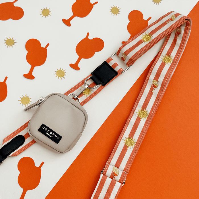 A orange and beige stripe bag strap, with embroidered drink and sun graphics. Attached is a small beige pouch for dog treats.
