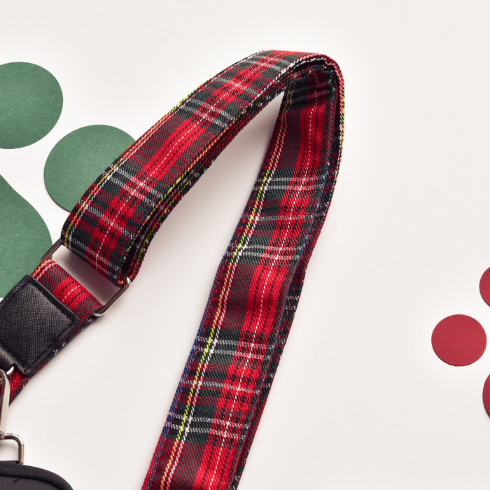 Tartan Cocopup London bag strap with silver hardware, displayed on green and red paper circles on a white background.