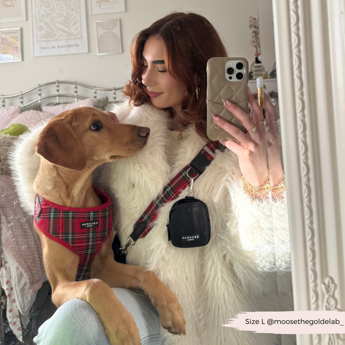 Woman in a white fur coat takes a mirror selfie with her brown dog, showing a red tartan Cocopup London bag strap.