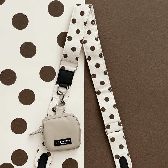 Small beige bag with a polka dot strap on a brown and white polka dot background