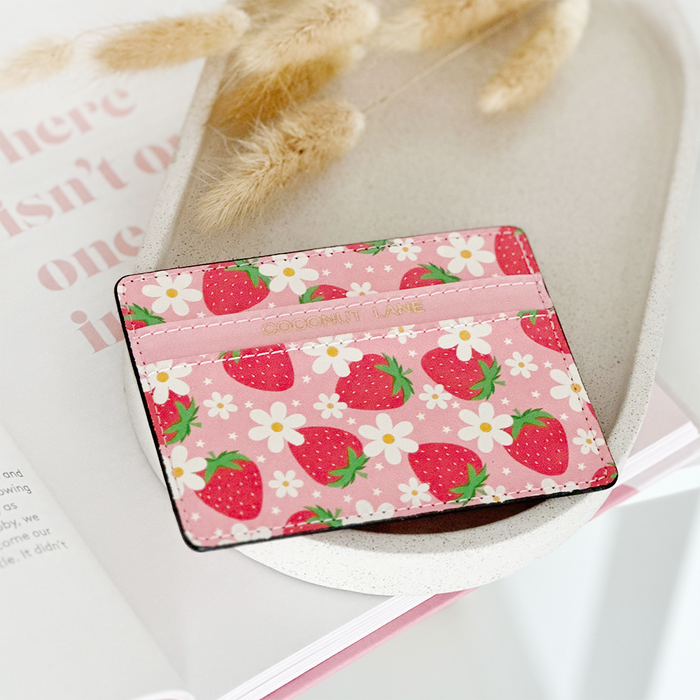 Pink strawberry-patterned card holder on a white dish, set against a pink magazine background.
