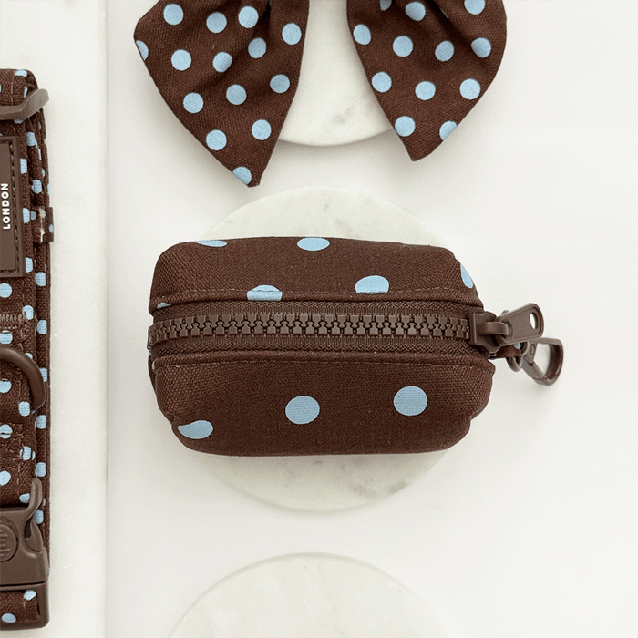 A brown poop bag holder, for dog poo bags, with light blue polka dot design. Featuring brown hardware.