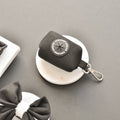 Black Aviator Poop Bag Holder by Cocopup London on a white dish next to a black bow.