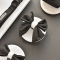 Black aviator-style sailor bow tie and black dog collar by Cocopup London displayed on white plates and marble slab.