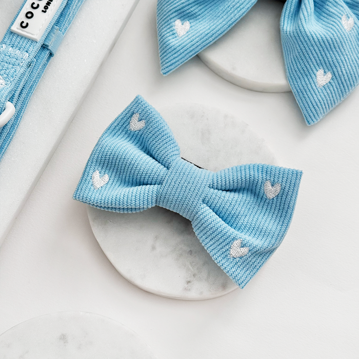 Blue cord bow tie with heart pattern from Cocopup London, displayed on marble alongside matching pet accessories.