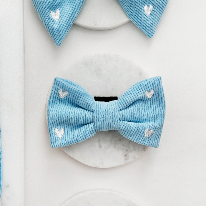 Blue cord dog bow tie with white heart pattern, displayed on a white marble surface.