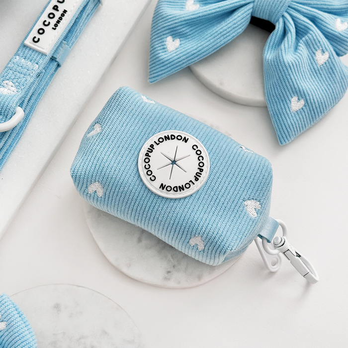 Light blue cord poop bag holder with white hearts by Cocopup London, next to a matching bow.