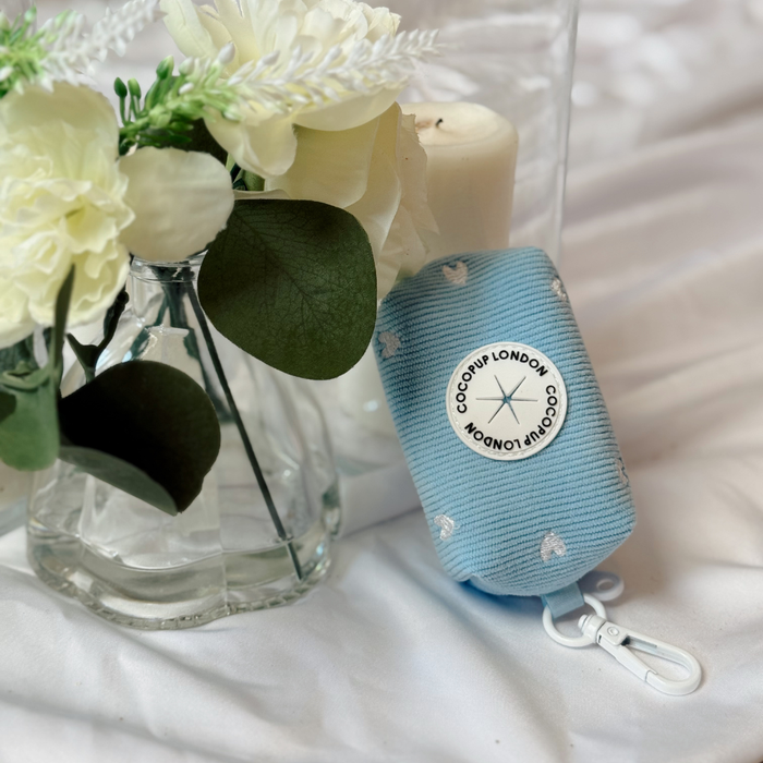 Blue cord Heartstrings poop bag holder with white heart pattern, placed on a white surface with floral decoration.