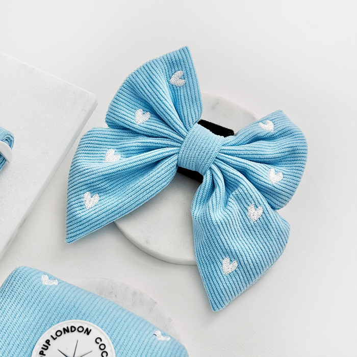 Blue corduroy sailor bow tie with heart pattern for dogs, displayed on a round base against a white background.