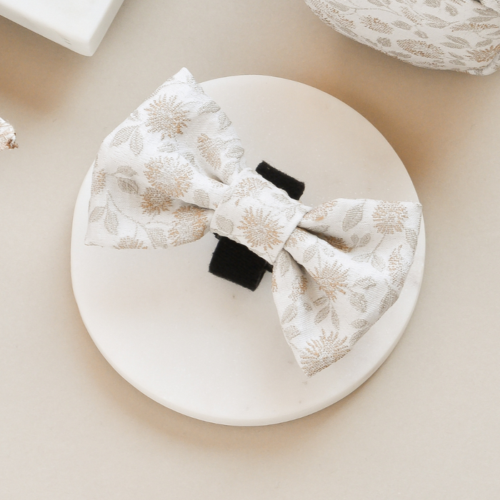 Garden Meadow patterned bow tie clipped to a black hair clip, shown on a round white platform.