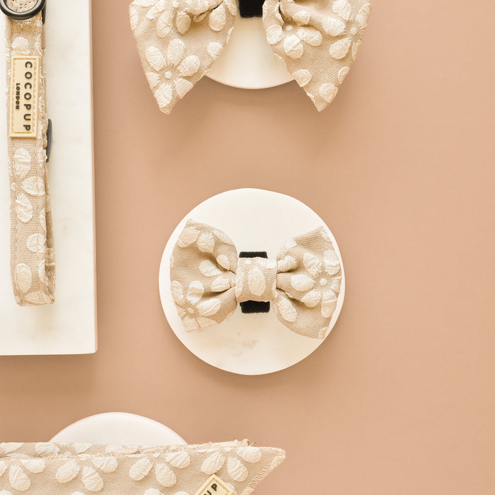 Mocha floral bow tie and matching leash in a flat lay on a tan background.