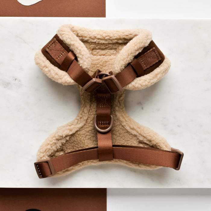 A stylish Brown Aviator Adjustable Neck Harness by Cocopup London lies on a marble background. This comfortable pet harness is made of soft, beige fleece with brown adjustable straps and buckles. Two metal rings are attached for leash connection, making it an ideal aviator adjustable neck harness.