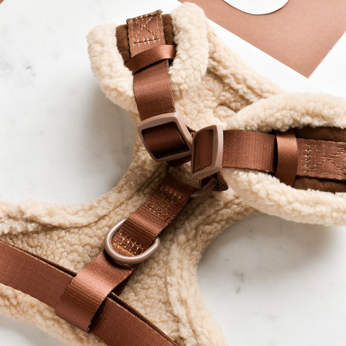 A close-up of a Cocopup London Brown Aviator Adjustable Neck Harness, a cozy fleece-lined and stylish dog harness featuring adjustable straps and metal buckles, placed on a white marble surface. The harness boasts a soft, padded interior for added comfort and is crafted with durable stitching.