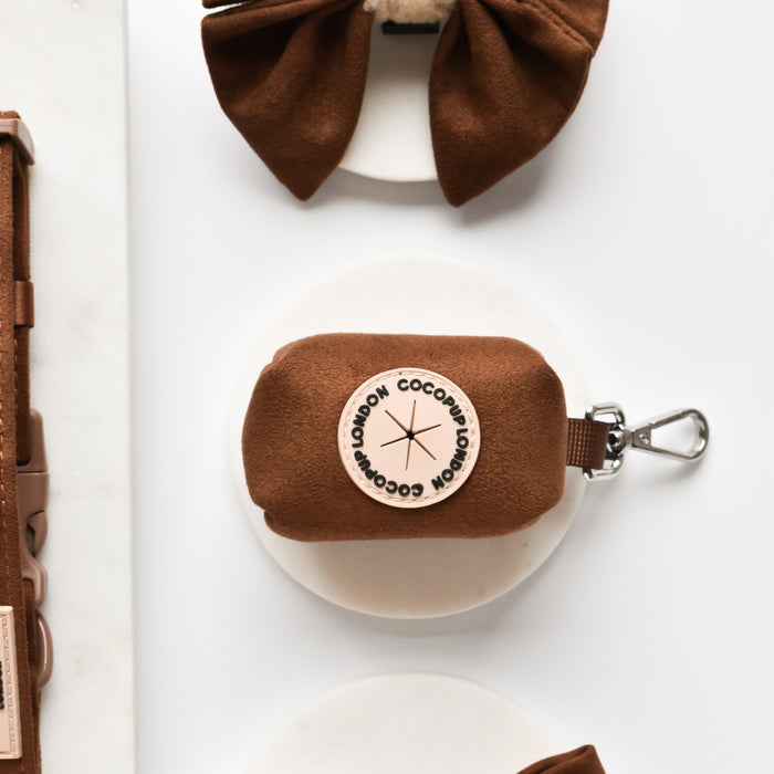 Brown Aviator Poop Bag Holder by Cocopup London with a round label and metal clip on a white background.