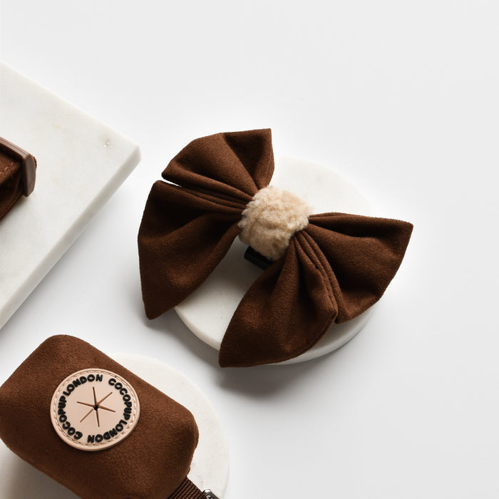 Brown aviator sailor bow tie with beige center on marble, beside brown faux suede dog accessories.