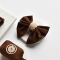 Brown aviator sailor bow tie with beige center on marble, beside brown faux suede dog accessories.