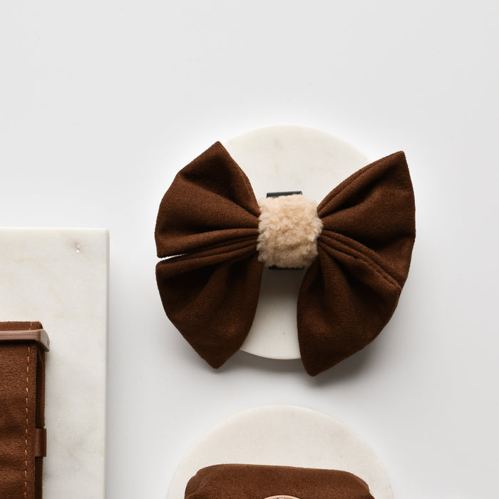Brown aviator-style sailor bow tie with beige fuzzy trim, displayed on a round white surface.